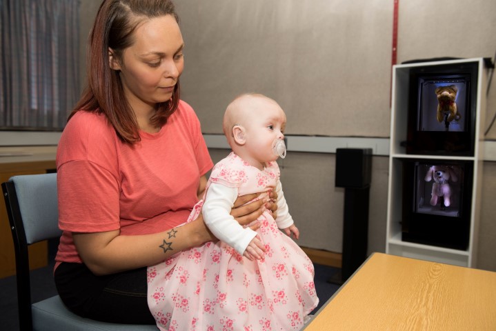 A baby in a dress is sat on their mothers knee