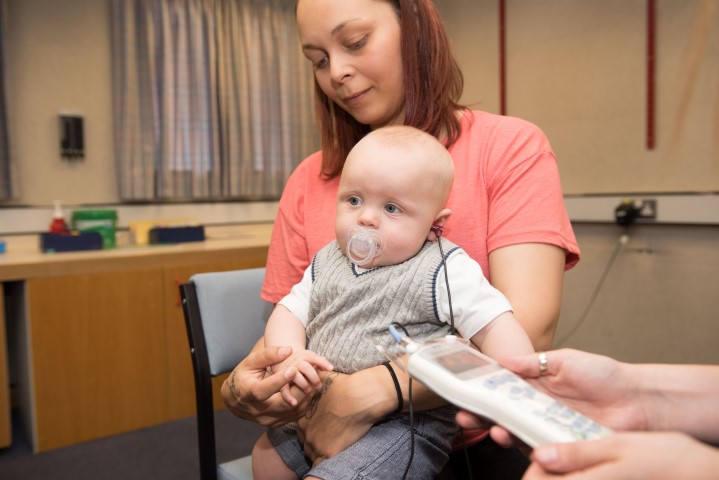 A baby sits on their mothers knee while having a hearing test