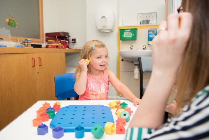 A happy little girl holds an object to her ear and listens to it