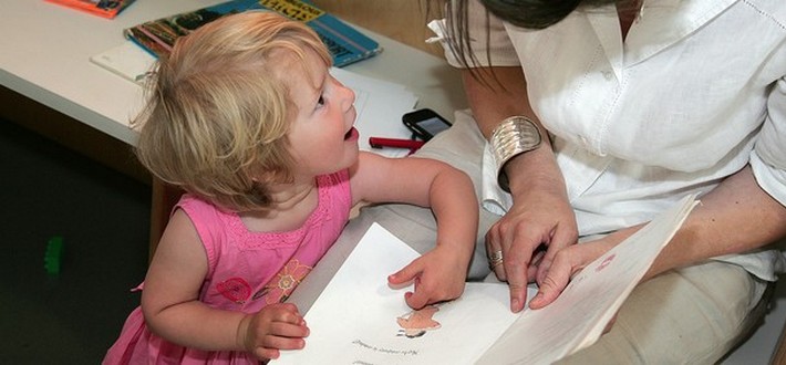child looking up at adult pointing at book together