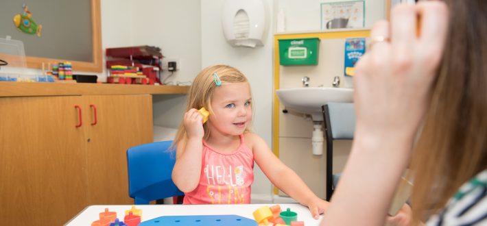 A happy little girl holds an object to her ear and listens to it