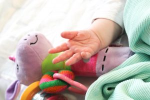 A baby's hand touching their purple teddy