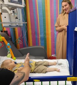 baby Edward laid in a cot with dad next to him and mum looking down smiling