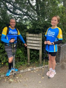 Molly wearing The Childrens Hospital Charity blue and yellow tshirt next to a sign for the Tissington Trail with hiking poles and trainers