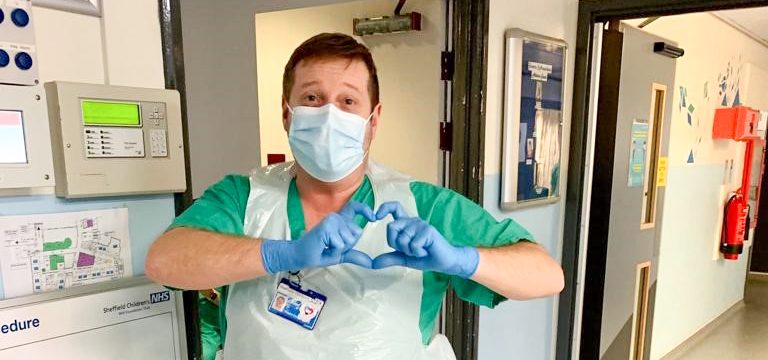happy theatres staff in scrubs, apron, blue gloves and mask making a love heart shape with hands