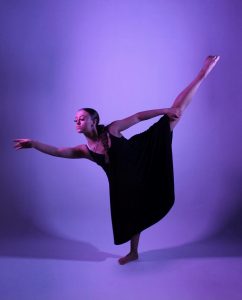 girl dancing with purple background and leg in the air behind her