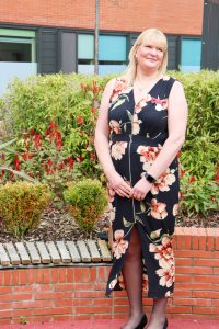 Adele Hague with floral dress on with red bricks and green bushes in the background